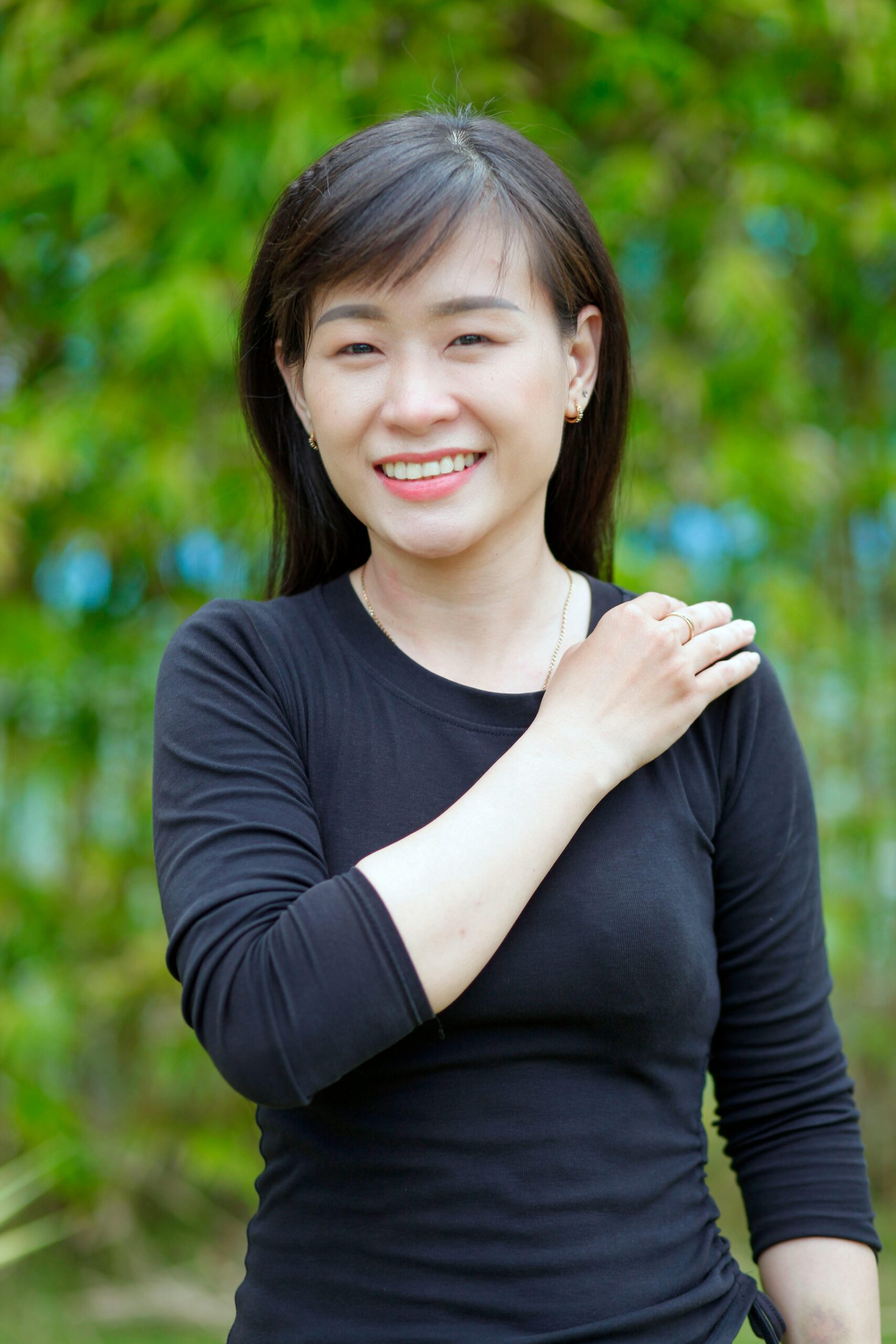 A cheerful woman with black hair, posing outdoors, exuding confidence and warmth.