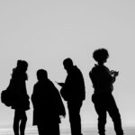 Black and white silhouette of four people communicating outdoors during daytime.