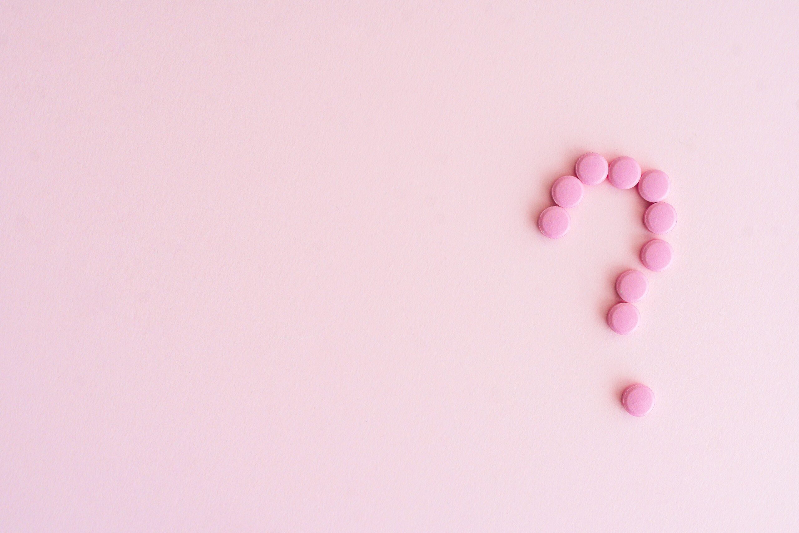 A question mark created from pink pills on a light pink surface, symbolizing uncertainty in health decisions.